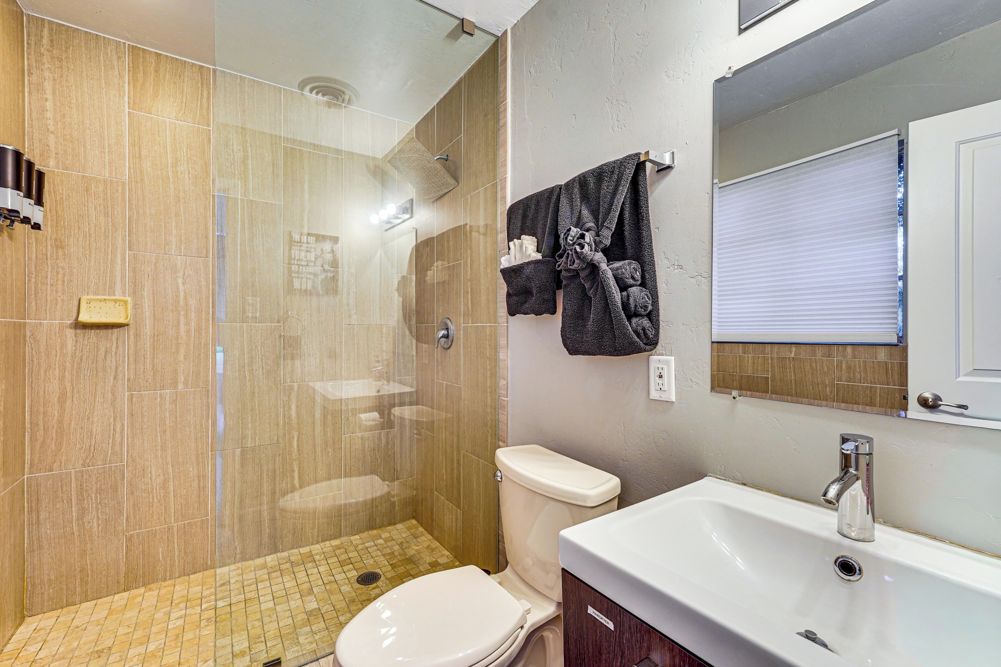 A bathroom with a glass-enclosed shower, a toilet, and a sink with a mirror above it.