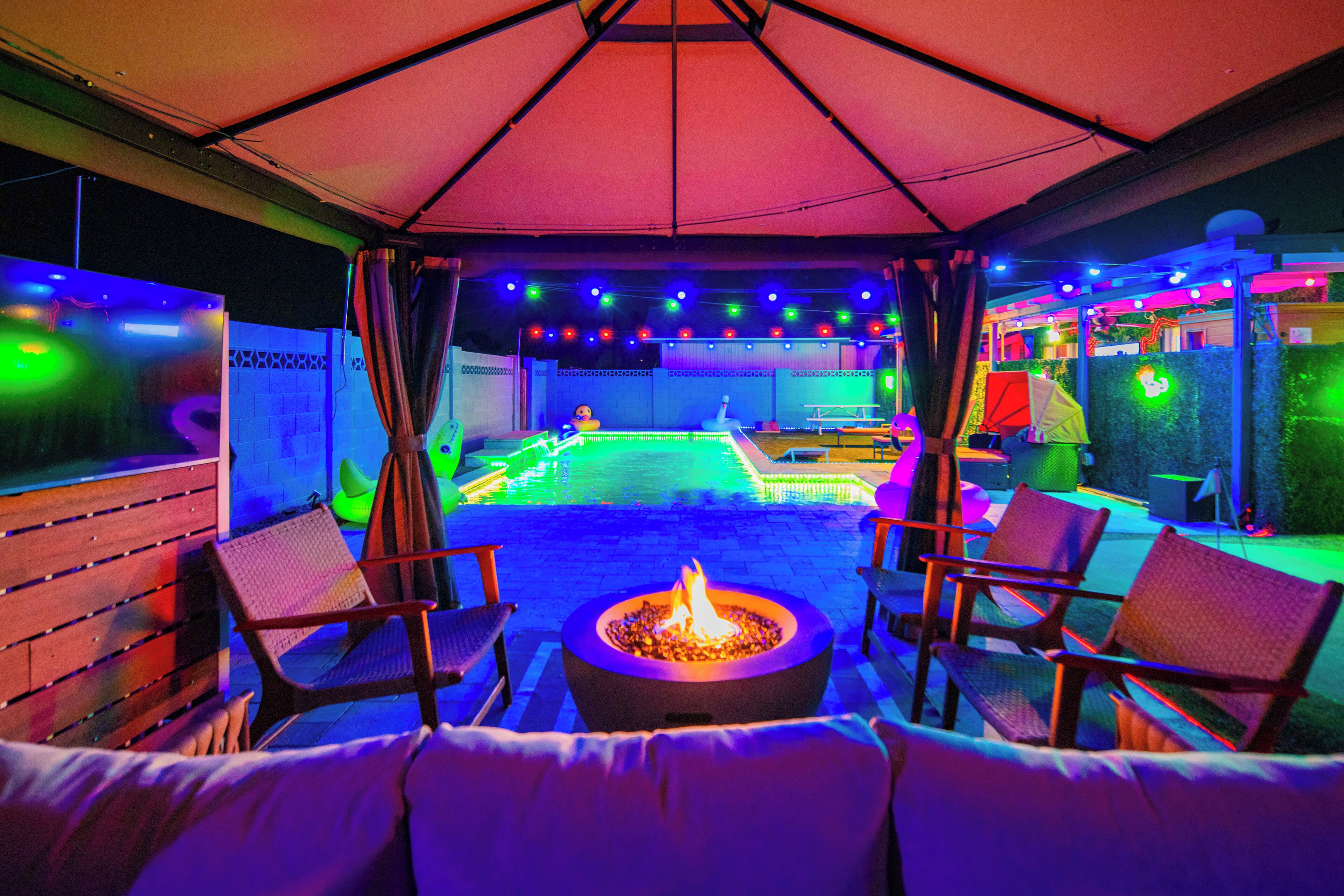 Un patio al aire libre con un hogar para fuego, asientos e iluminación de colores.