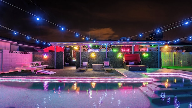 Ett poolområde med ett staket som är upplyst med neonljus, solstolar och en neonskylt.