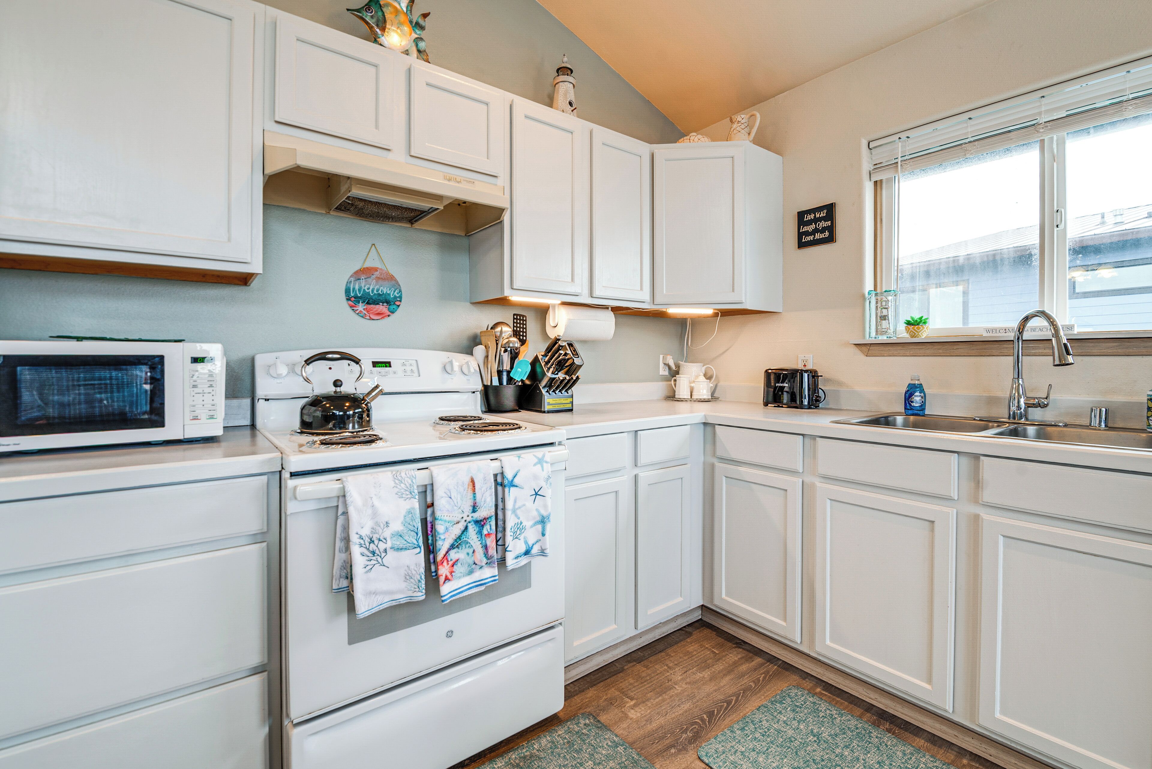 A kitchen with white cabinets, a microwave, stove, and a sink.