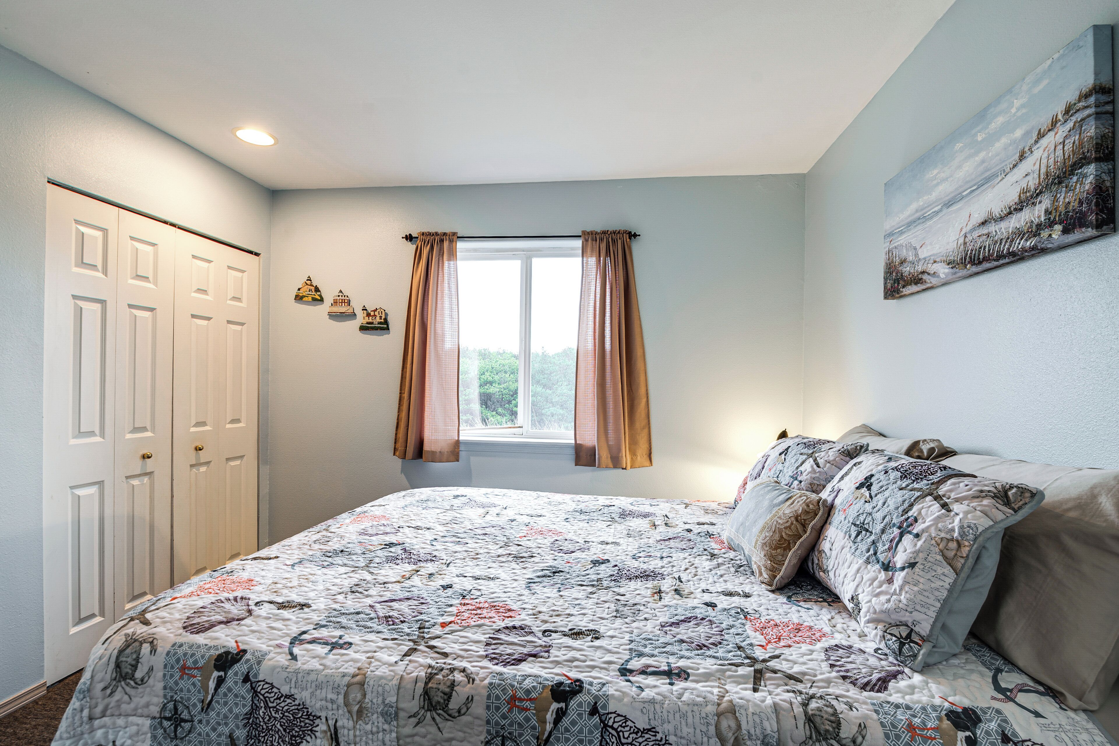 A bedroom with a large bed, a window with curtains, a painting on the wall, and a closet.