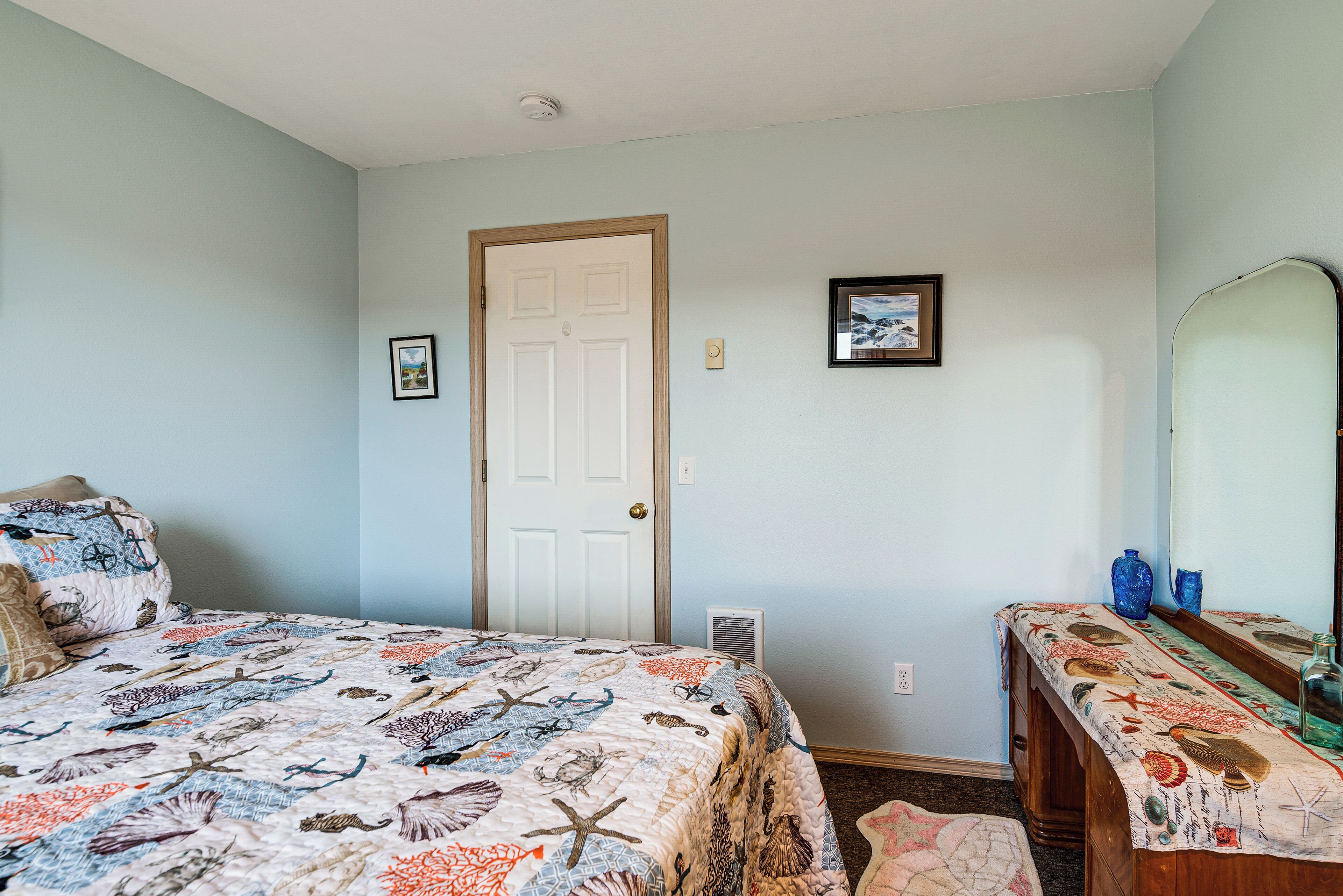 A bedroom with a bed, a dresser, a door, and a framed picture on the wall.