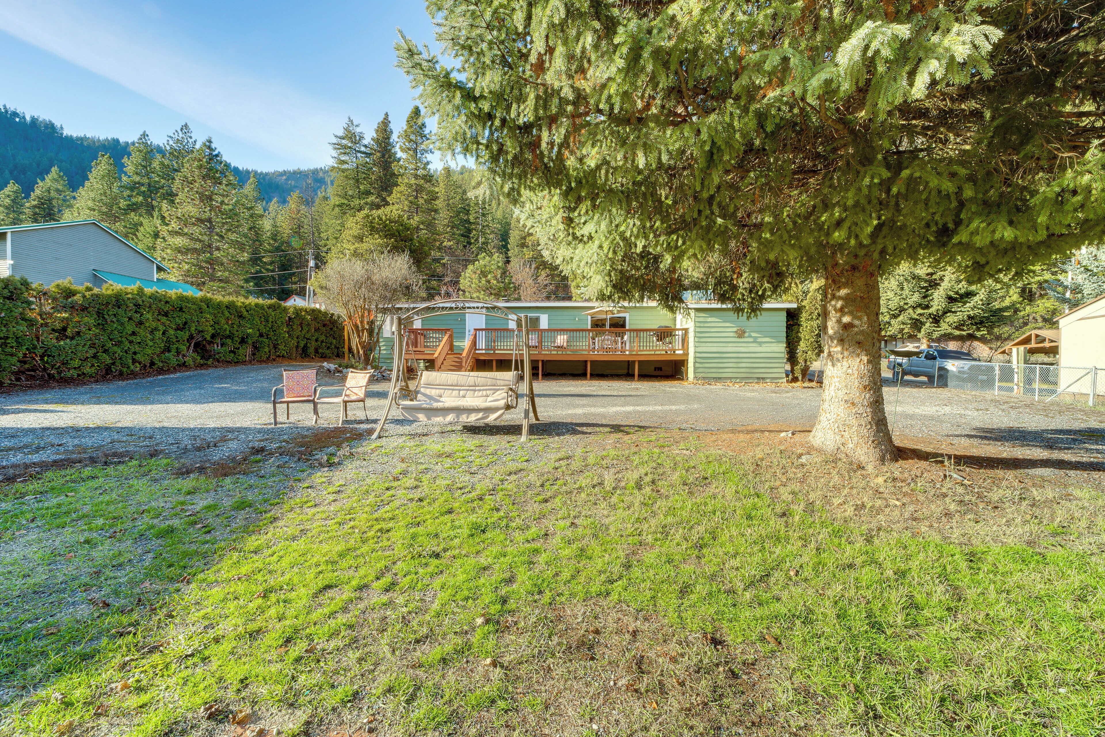 A cabin with a deck and a covered porch, surrounded by trees and a mountain backdrop.