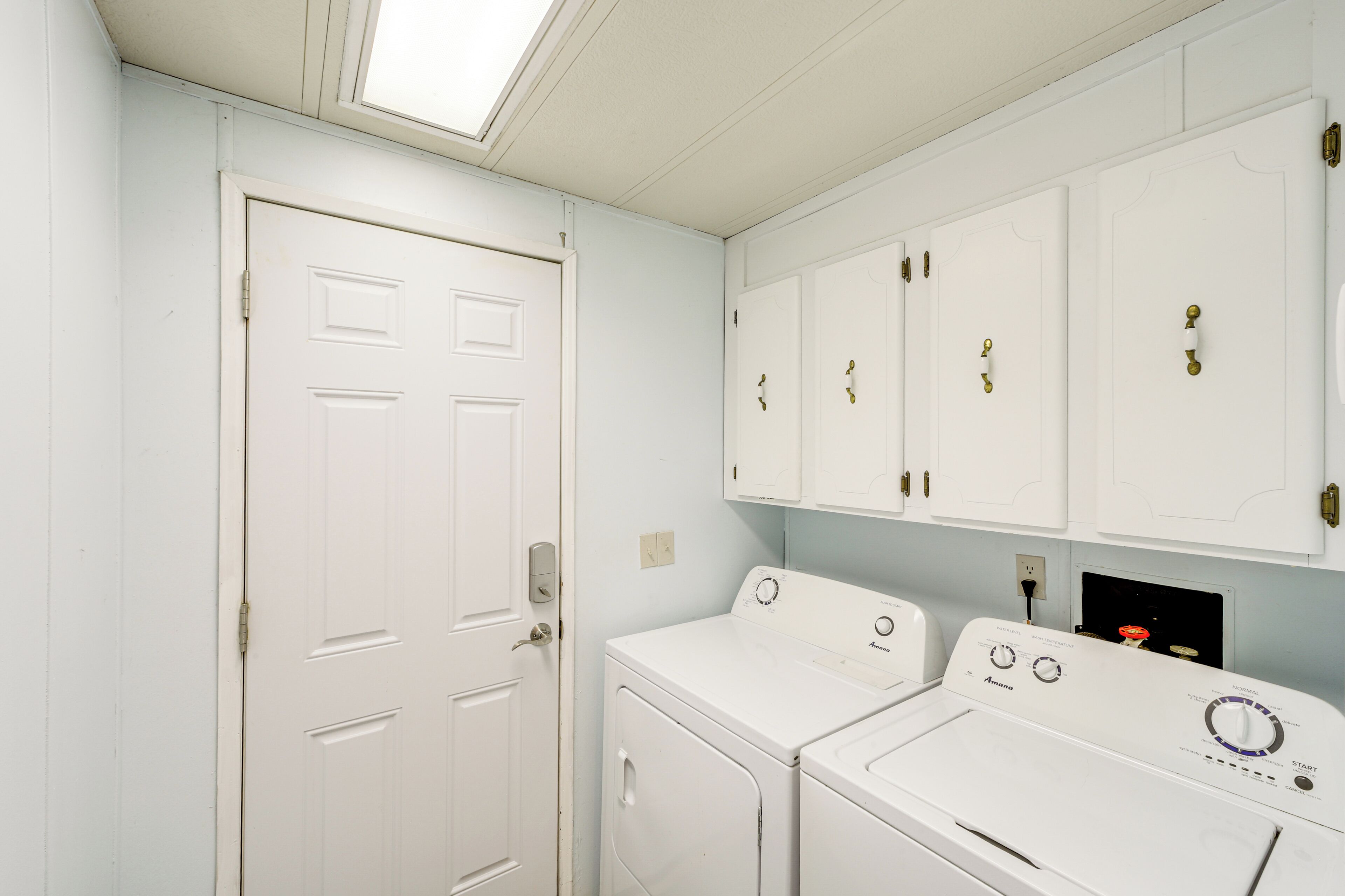A laundry room with two white washers and dryers, white cabinets, and a skylight.