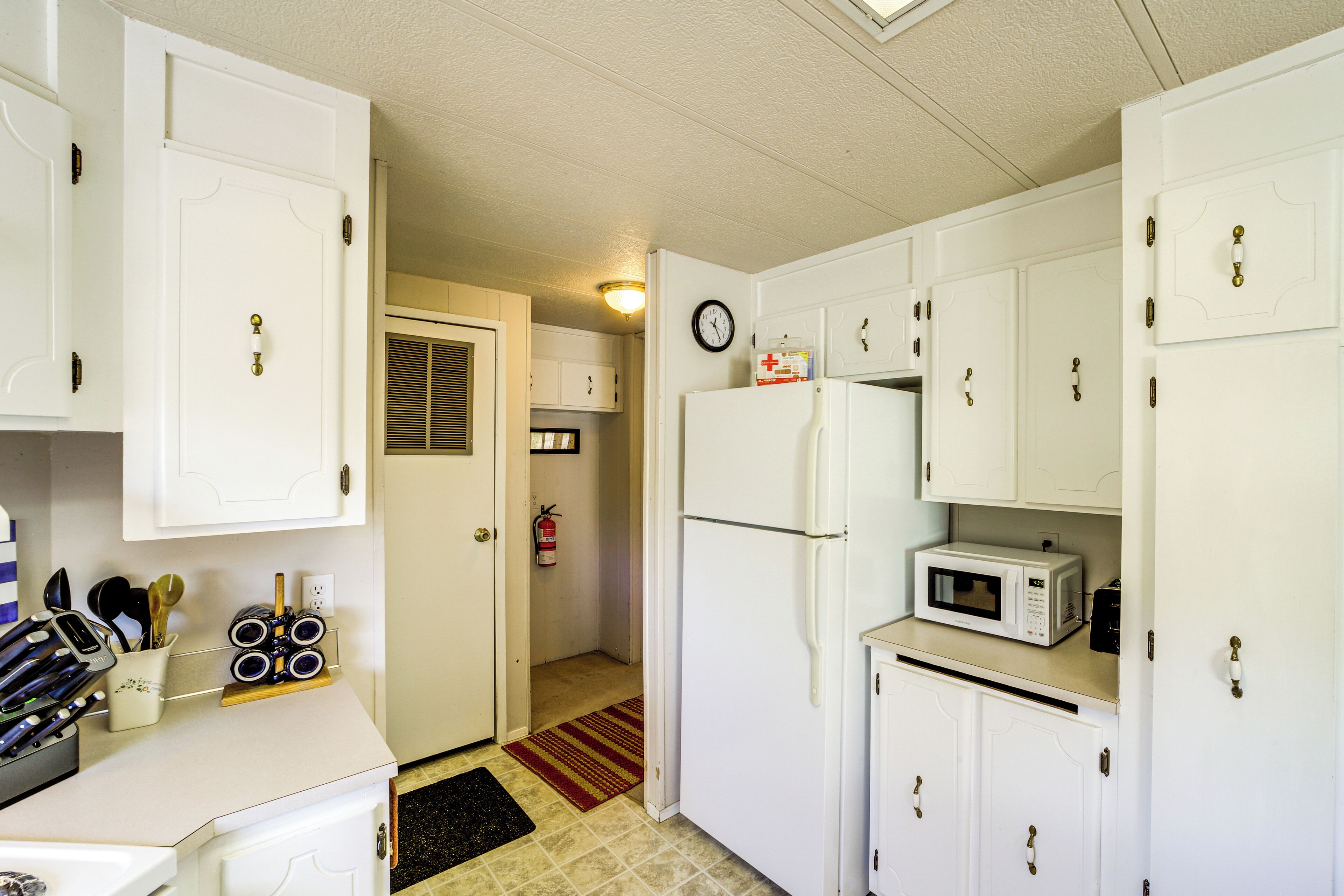 A compact kitchen with white cabinets, a refrigerator, a microwave, and a fire extinguisher.