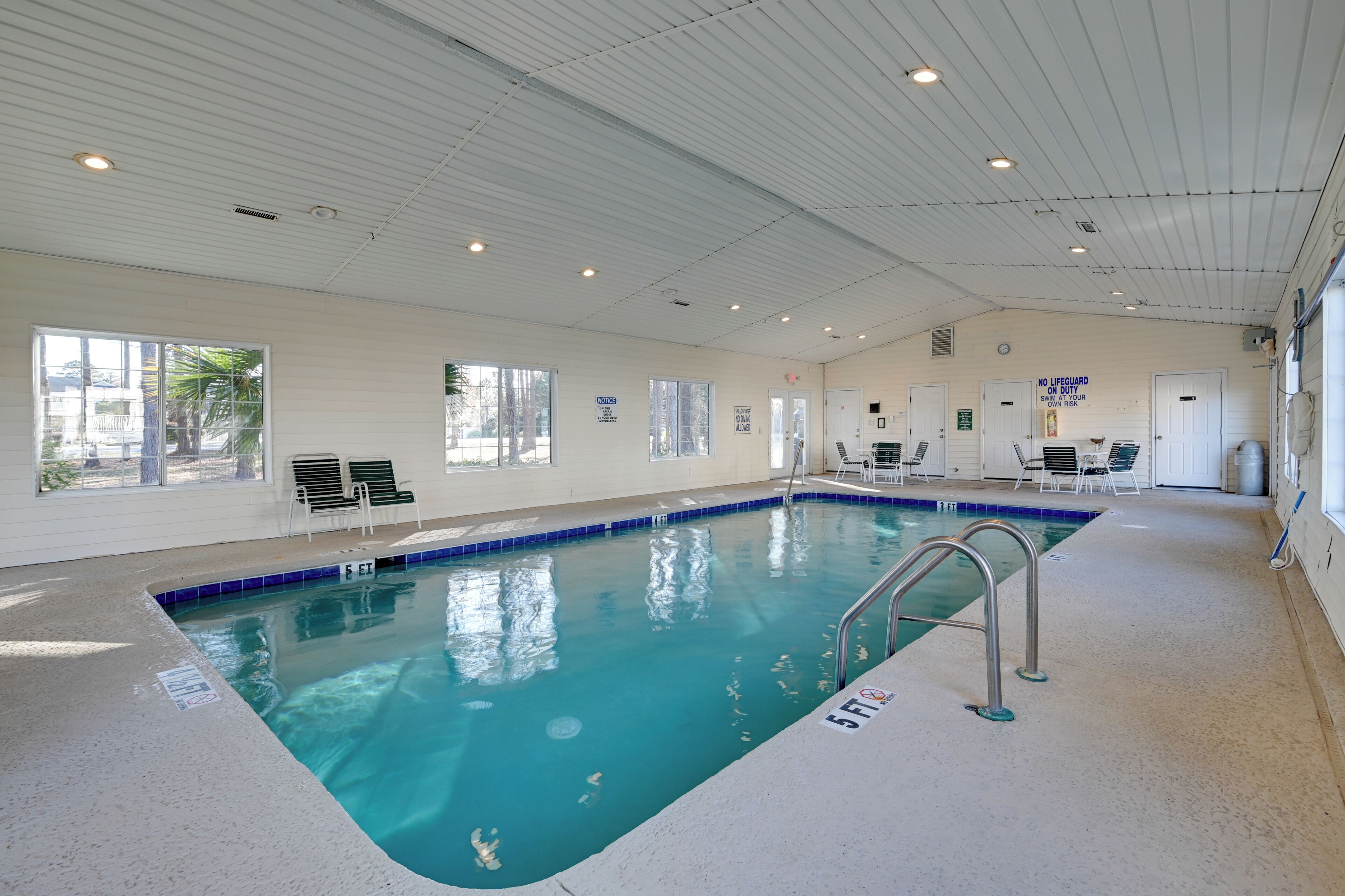 An indoor swimming pool with clear blue water, a lifeguard station, and a no lifeguard sign.