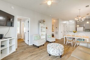 A spacious living room with a TV, white sofas, a dining area with a table and chairs, and a kitchen with white cabinets and a chandelier. - Myrtle Beach Condo w/ Pool & Golf Access (Myrtle Beach)