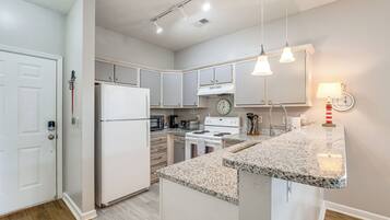 A modern kitchen with white appliances, granite countertops, and pendant lighting.