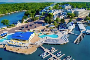 Ein Luftbild zeigt einen Urlaubsort mit einer Marina, Schwimmbecken und einem großen Gebäude mit blauem Dach.