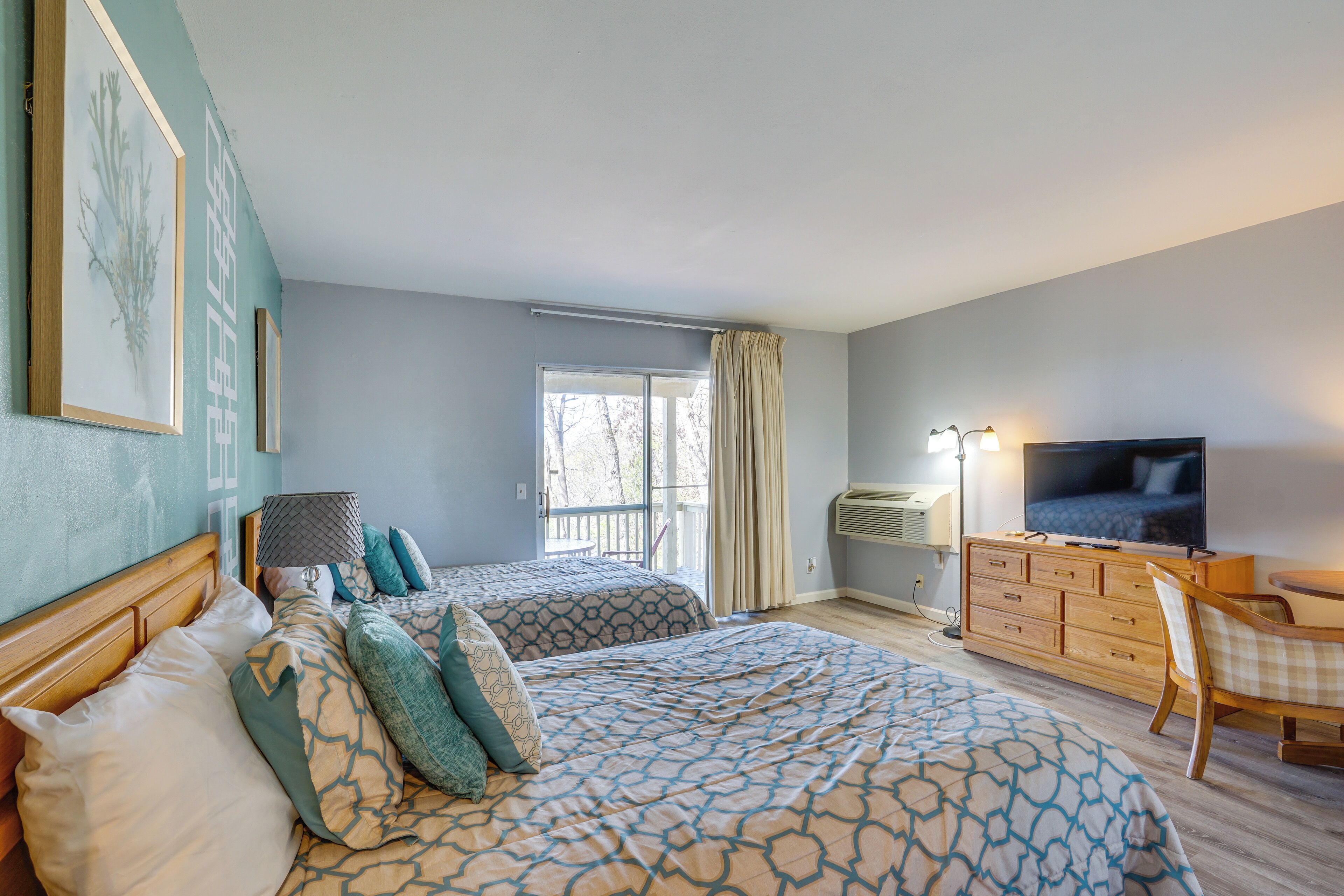 A hotel room with two beds, a television, a desk with a chair, and a window with curtains.