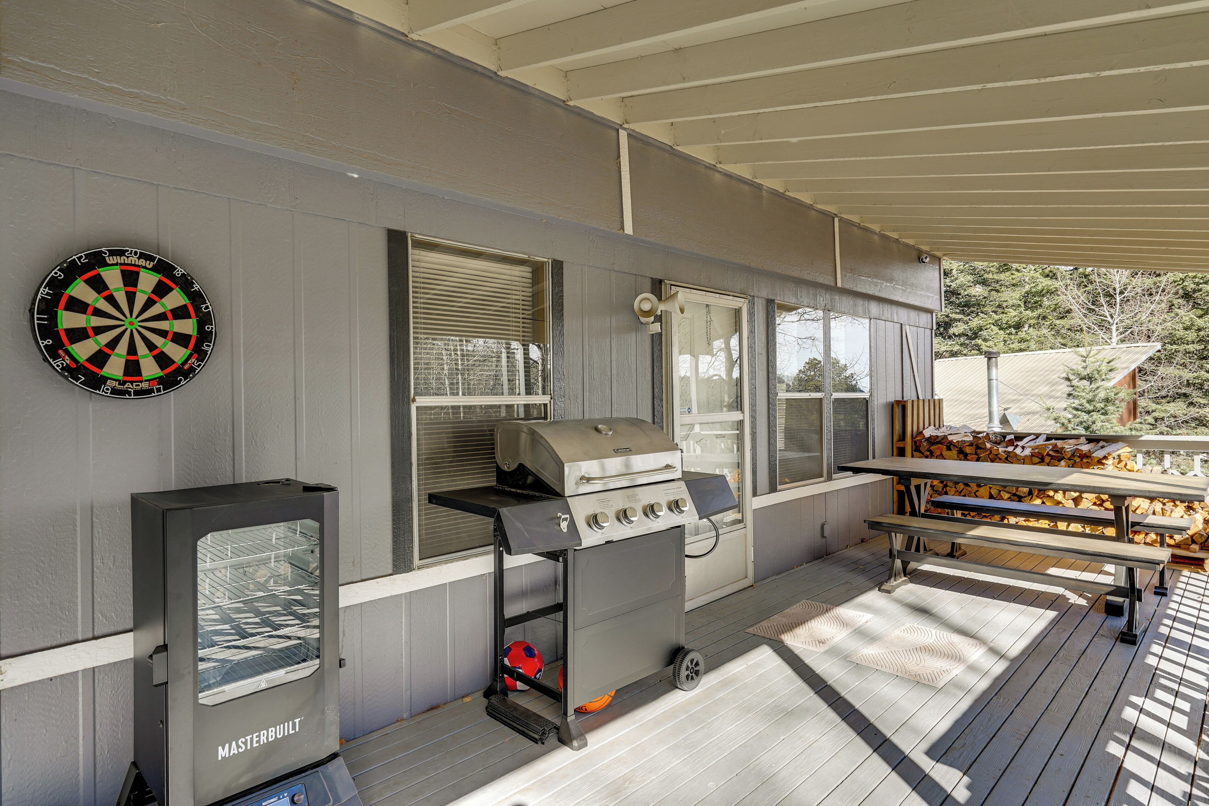 A covered patio area with a grill, a dartboard, and a table with benches.