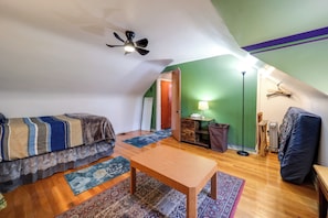 A small, cozy attic bedroom with a bed, a wooden table, a floor lamp, and a ceiling fan.