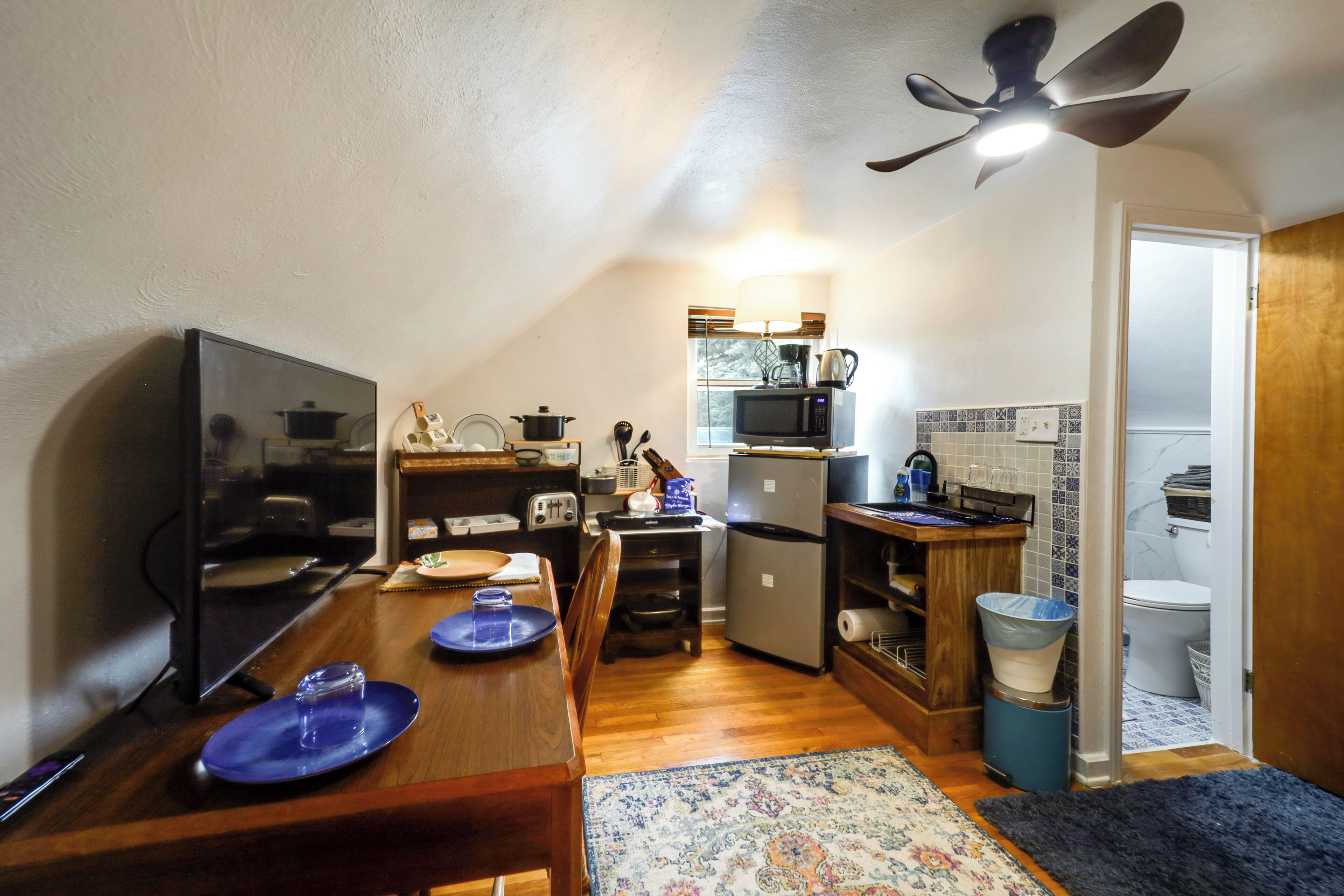 A compact kitchen with a dining table, microwave, refrigerator, and a ceiling fan.