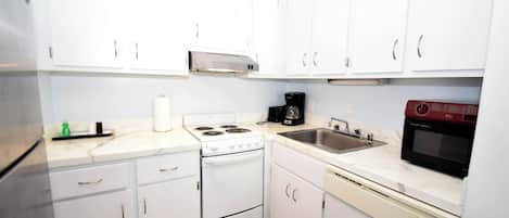A compact kitchen with white cabinets, a stove, a microwave, a coffee maker, and a dishwasher.