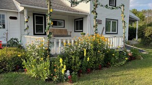 Een wit huis met een veranda, omgeven door een tuin vol diverse bloemen en een standbeeld.