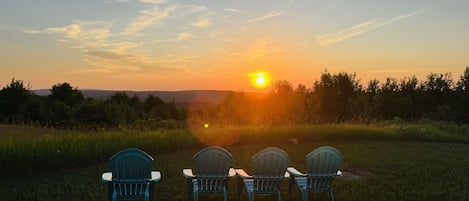 Three chairs facing a sunset over a grassy field.