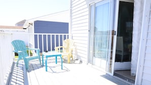 A covered outdoor deck with two chairs and a table, a sliding glass door, and a white fence. - West Ocean City Vacation House Rental in Quiet Residential Neighborhood (Ocean City)