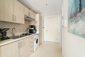 A modern kitchen with light wood cabinets, a stainless steel sink, a microwave, and a washing machine. - Stylish Studio with Beach Access |Palm Jumeirah (Dubai)