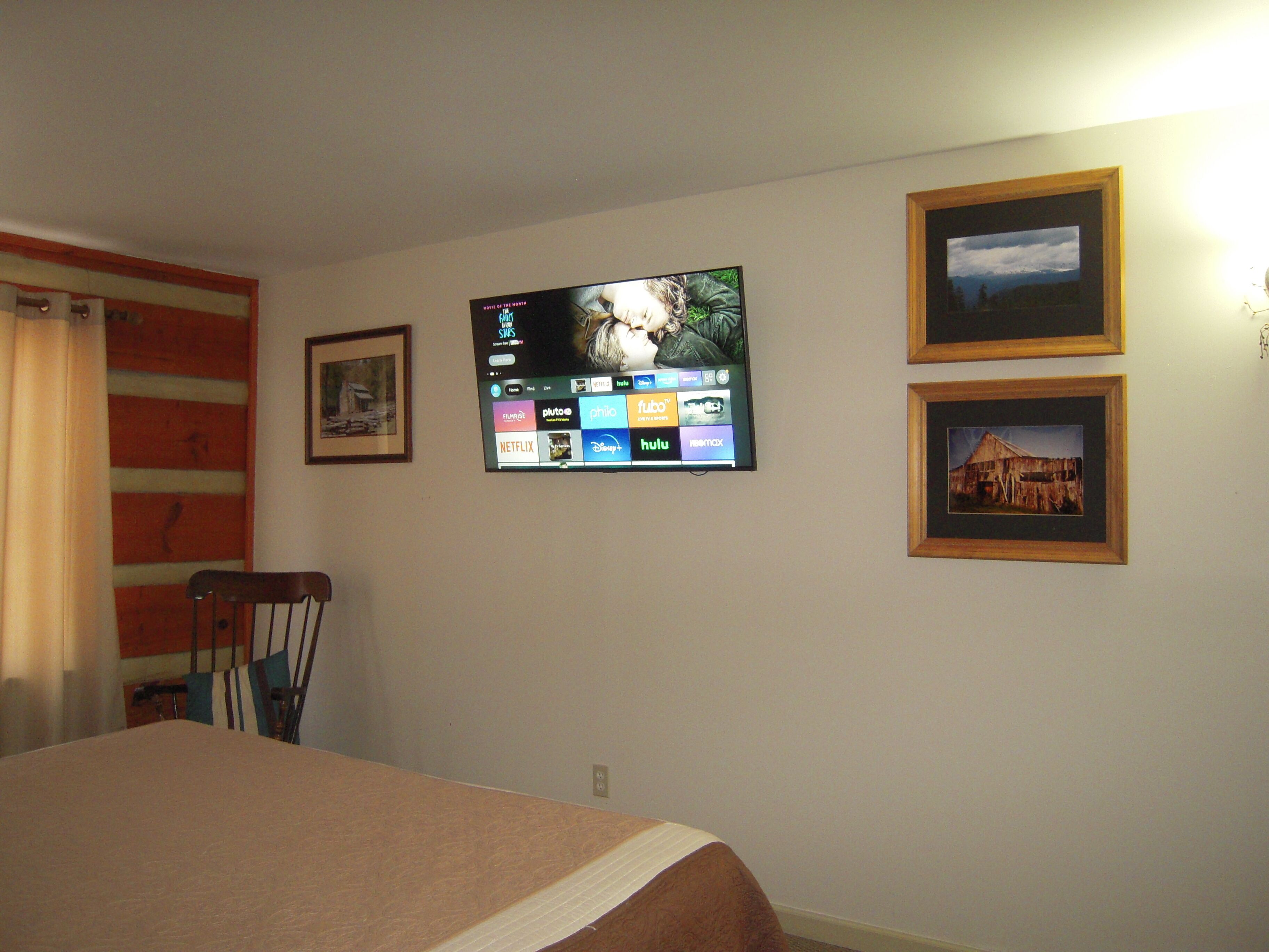 Camera d'albergo con un letto, una televisione a muro che mostra diversi servizi di streaming e due quadri appesi.