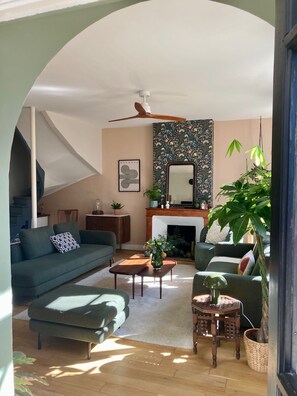 A living room with a sofa, coffee table, and a fireplace. There is a staircase to the left and a large plant on the right. - A Toulouse woman of character (Lavernose-Lacasse)