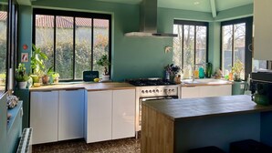 Une cuisine moderne dotée d’une cuisinière à gaz, de meubles blancs et d’une grande fenêtre donnant sur un jardin.