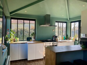 A modern kitchen with a gas stove, white cabinets, and a large window overlooking a garden. - A Toulouse woman of character (Lavernose-Lacasse)