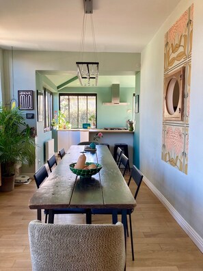A dining area with a long table, chairs, and a bowl of fruit. There are potted plants and a hanging light fixture. - A Toulouse woman of character (Lavernose-Lacasse)