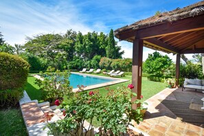 Ein Poolbereich mit Pergola, Liegestühlen und einem Garten mit verschiedenen Pflanzen.