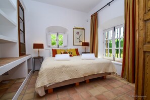 Quarto com cama, duas mesinhas de cabeceira, janela com cortinas e um quadro na parede.