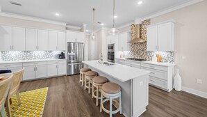 A modern kitchen with white cabinets, a large island, bar stools, and stainless steel appliances. - New! 5 minutes from Rosemary Beach! Bikes, Beach Gear, Game & Bunk Room, 8 Beds (Inlet beach)