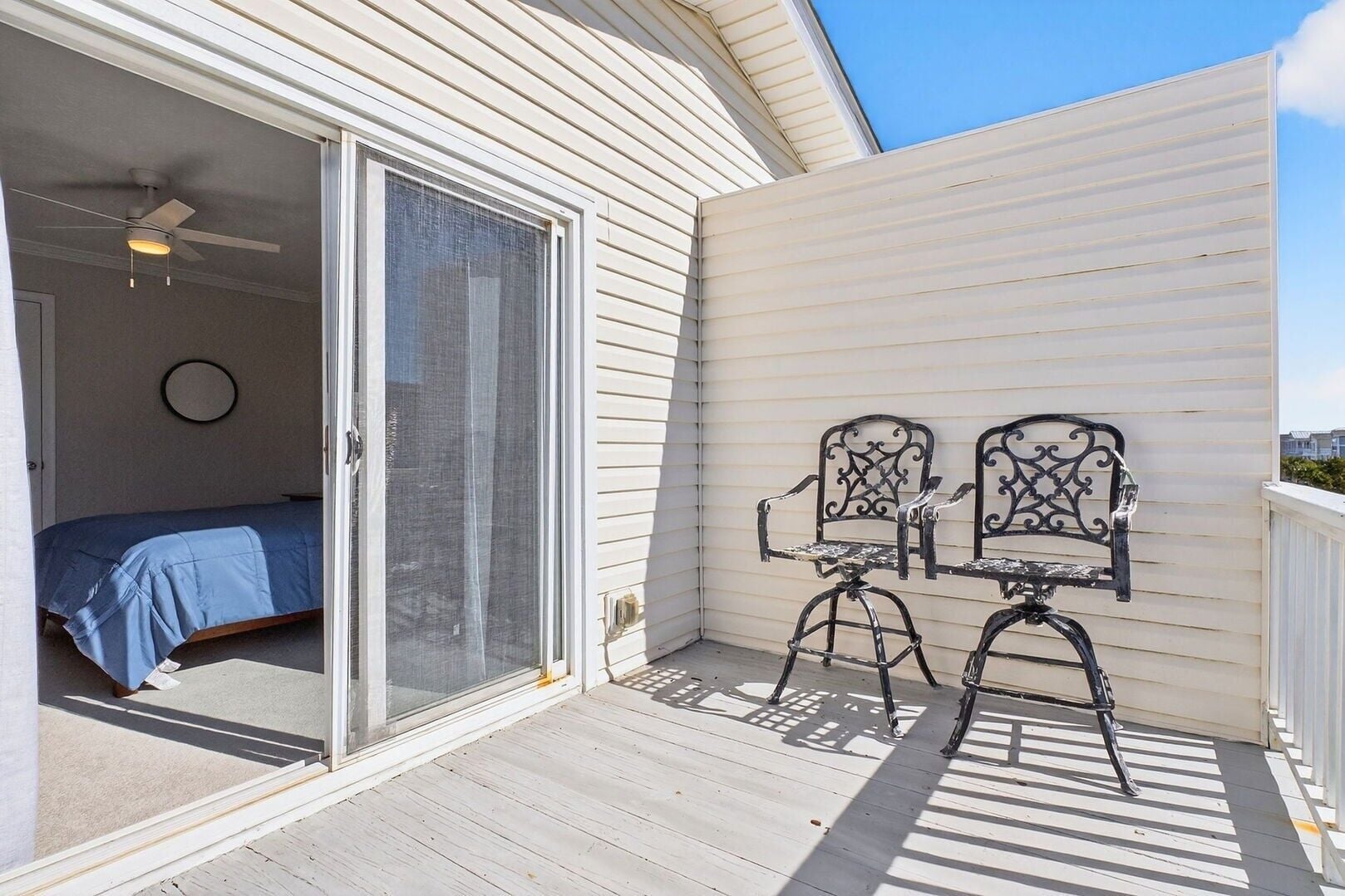 Une pièce avec un lit, une porte-fenêtre coulissante et deux chaises sur une terrasse en bois.