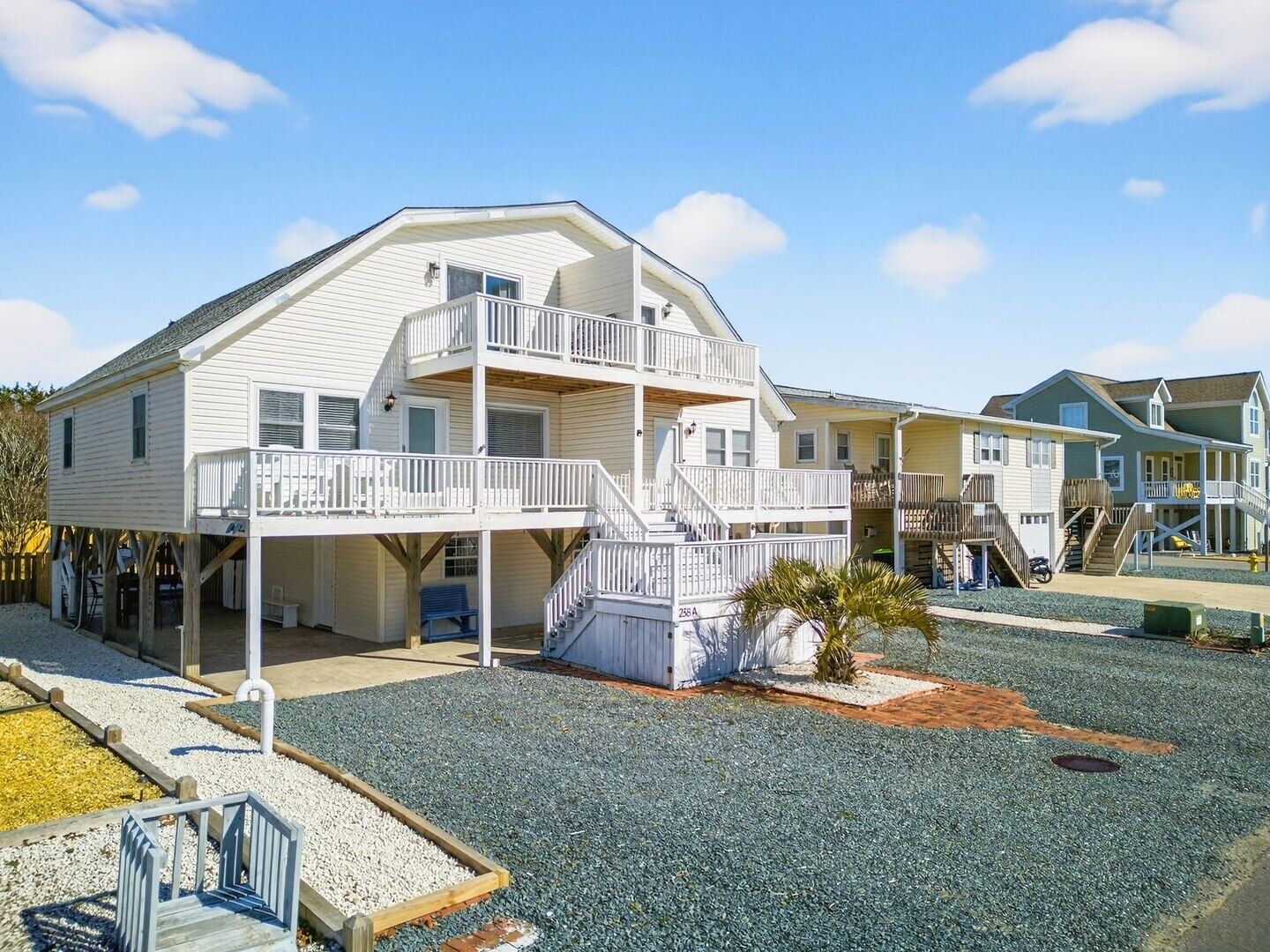 A multi-story beachfront property with a balcony, a small garden, and a clear sky.
