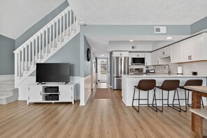 A modern kitchen with white cabinets, a central island with bar stools, and a built-in TV. - Luna By The Sea / 238 Brunswick Ave West 3 Bedroom Home (Supply)