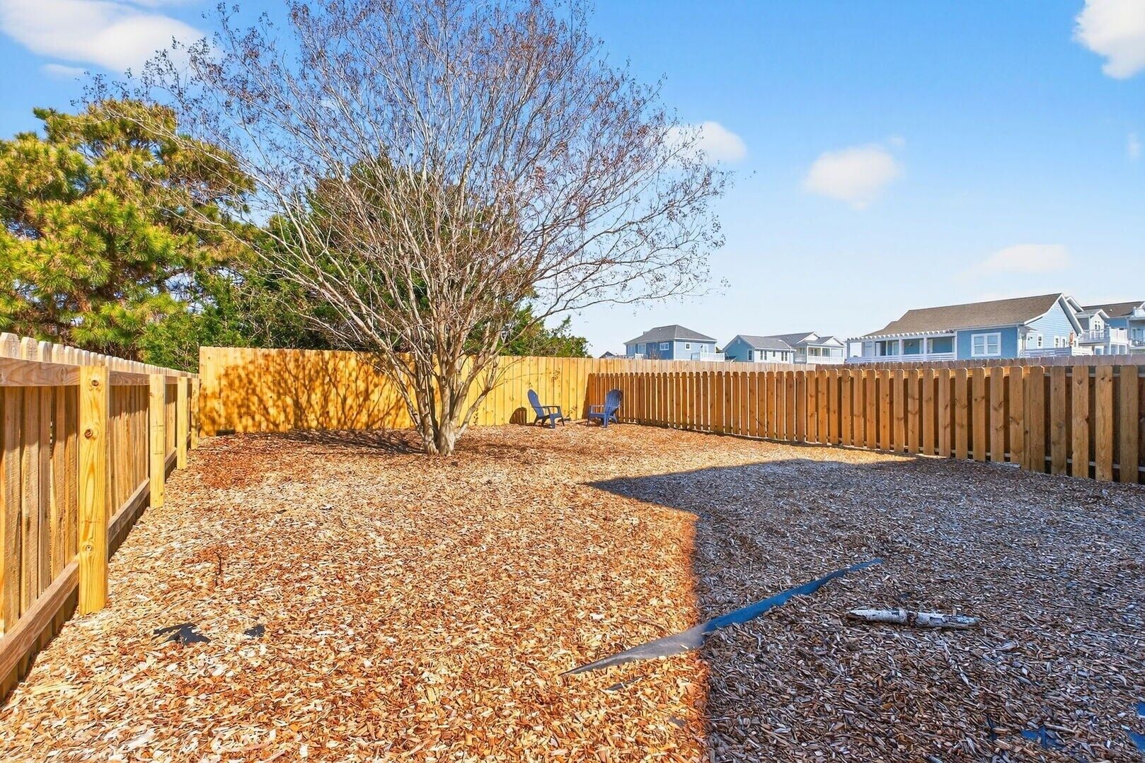 A backyard with a wooden fence, a tree, and a gravel area.
