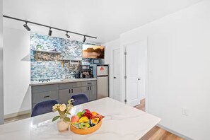 Una cocina moderna con salpicadero de azulejos azules y blancos, un refrigerador de acero inoxidable y un comedor con mesa y sillas de mármol.
