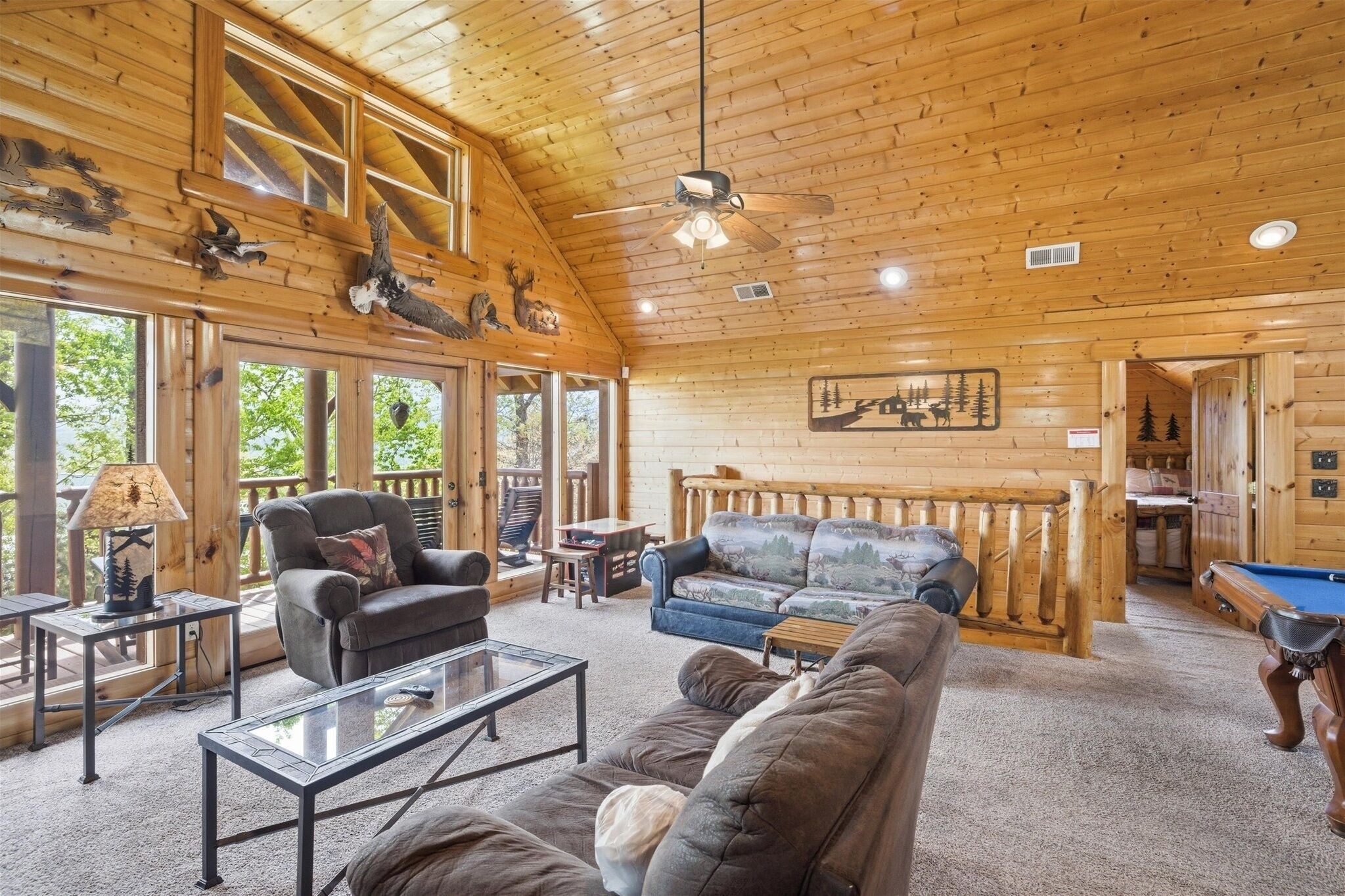 A wooden interior with a ceiling fan, a sofa, a coffee table, and a pool table.