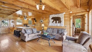 A log cabin interior with a wooden ceiling, a bear mural, two sofas, a coffee table, and a kitchen area. - A View To A Dream 4 Bedroom Home (Sevierville)