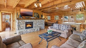 A log cabin interior with a stone fireplace, wooden furniture, and a large TV mounted on the wall. - A View To A Dream 4 Bedroom Home (Sevierville)