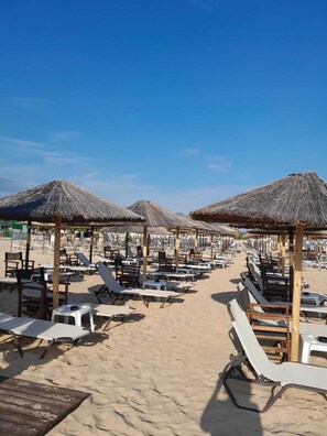 A beach with rows of sun loungers and thatched umbrellas. - Garden Apartment in Panorama Kariani with Free Parking & BBQ, Near the Sea (Paralia Ofriniou)