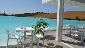 An outdoor dining area with white tables and chairs, overlooking a clear blue pool and a hilly landscape. - Alcazaba Lagoon Retreat for 4 (Casares)