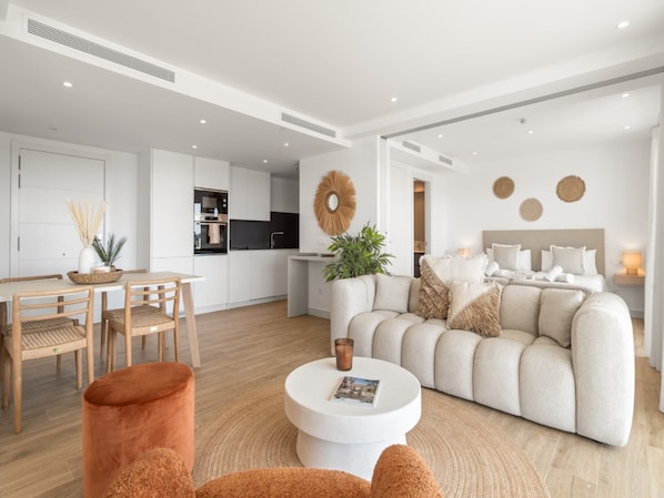 A modern interior with a dining area, a living room with a sofa and coffee table, and a kitchen in the background. - Alcazaba Lagoon Retreat for 4 (Casares)