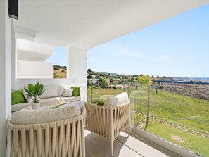 A modern balcony with a sofa and chairs, a potted plant, and a view of a rural landscape. - Alcazaba Lagoon Retreat for 4 (Casares)