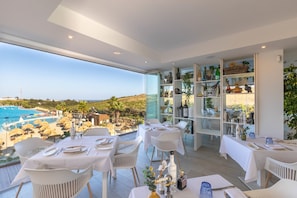 Comedor con mesas preparadas para dos, con vista a una piscina y un paisaje pintoresco.