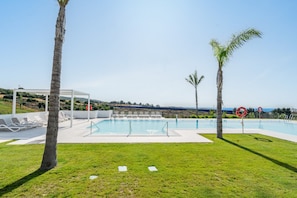 Zona de piscina con sillones, una pérgola y palmeras.