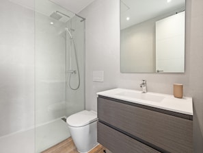 A modern bathroom with a glass shower enclosure, a white toilet, a vanity with a mirror, and a wooden cabinet. - Alcazaba Lagoon Retreat for 4 (Casares)