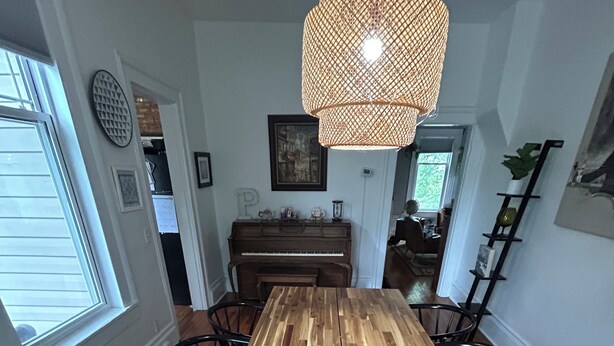 Comedor con mesa de madera, sillas negras, un piano y una lámpara colgante.