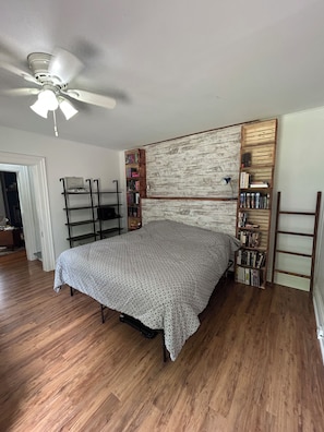 A bedroom with a bed, wooden floor, ceiling fan, and built-in bookshelves.