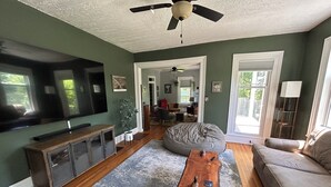 Una sala de estar con ventilador de techo, un sillón orejero grande, una mesa de centro de madera y un televisor.