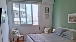 A bedroom with a bed, two chairs, a window, and a wall-mounted air conditioner. - Atlantic Avenue, Post 6, Incredible View  (Rio de Janeiro)