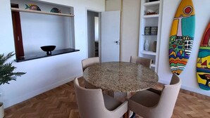 A dining area with a round table and chairs, wooden herringbone flooring, white walls, and a surfboard decoration. - Atlantic Avenue, Post 6, Incredible View  (Rio de Janeiro)